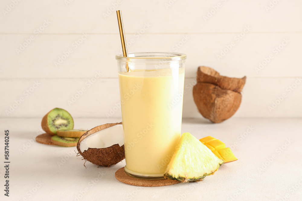 Glass of tasty pineapple smoothie, kiwi and coconut on table