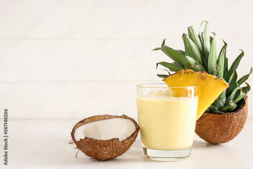 Glass of tasty pineapple smoothie and coconut on white table