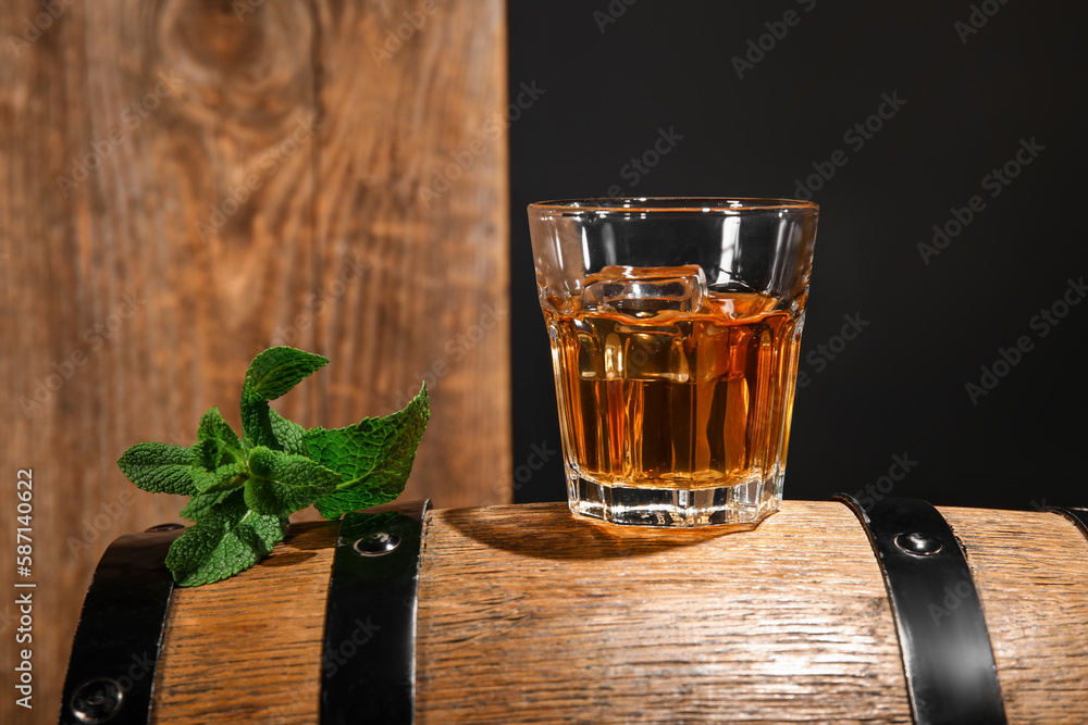 Glass of cold rum on barrel against wooden background