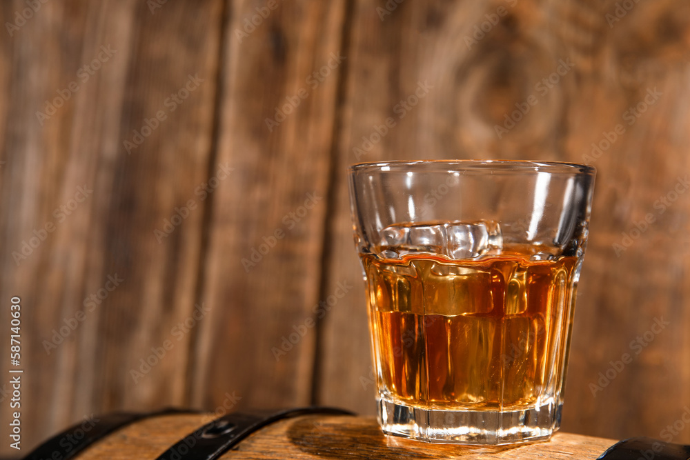 Glass of cold rum on barrel against wooden background