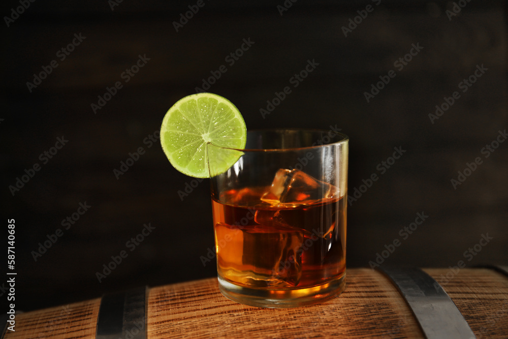 Glass of cold rum on barrel against wooden background