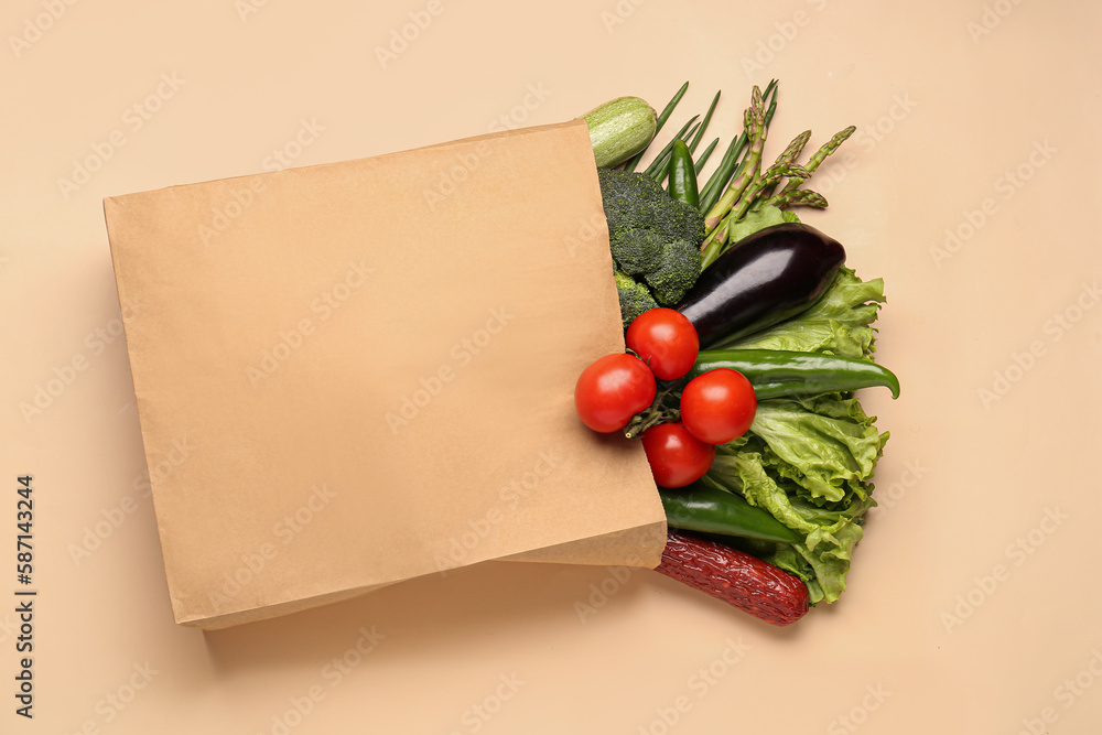 Paper bag with vegetables and sausage on beige background