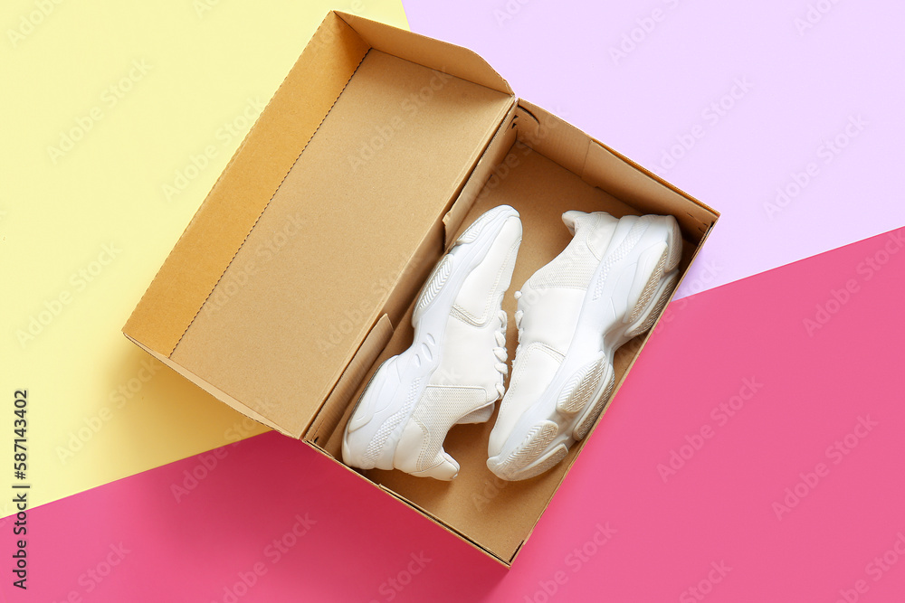 Cardboard box with sports shoes on color background