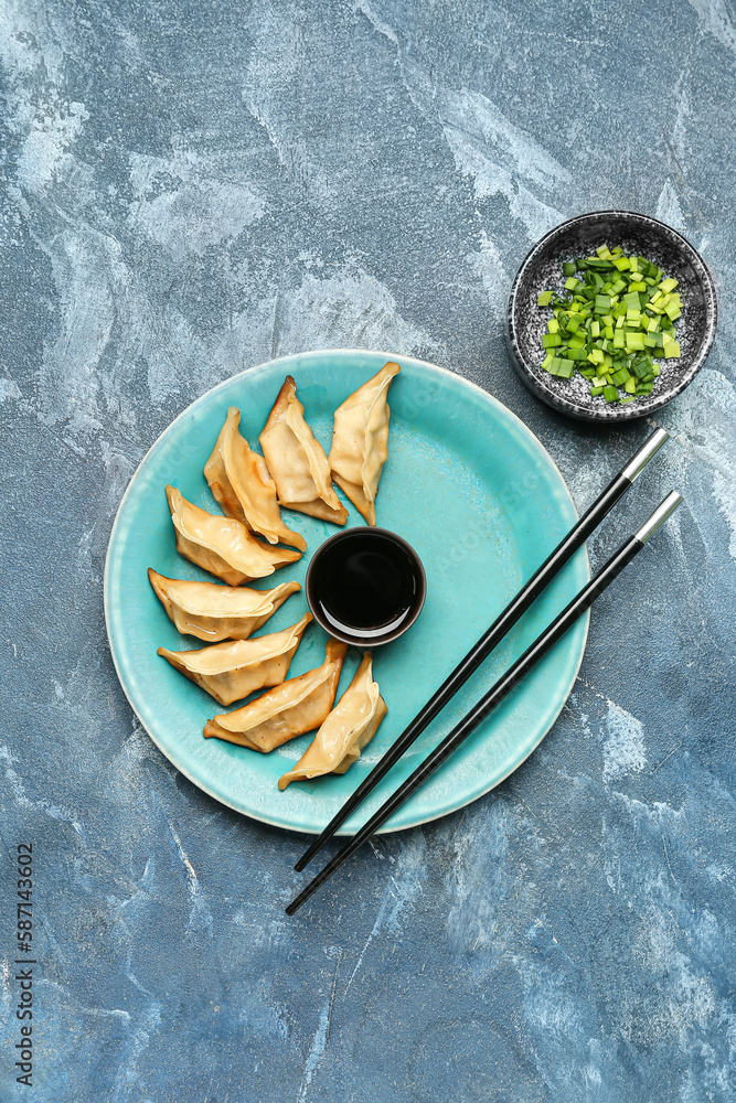 Plate with tasty Chinese jiaozi, green onion and sauce on blue background