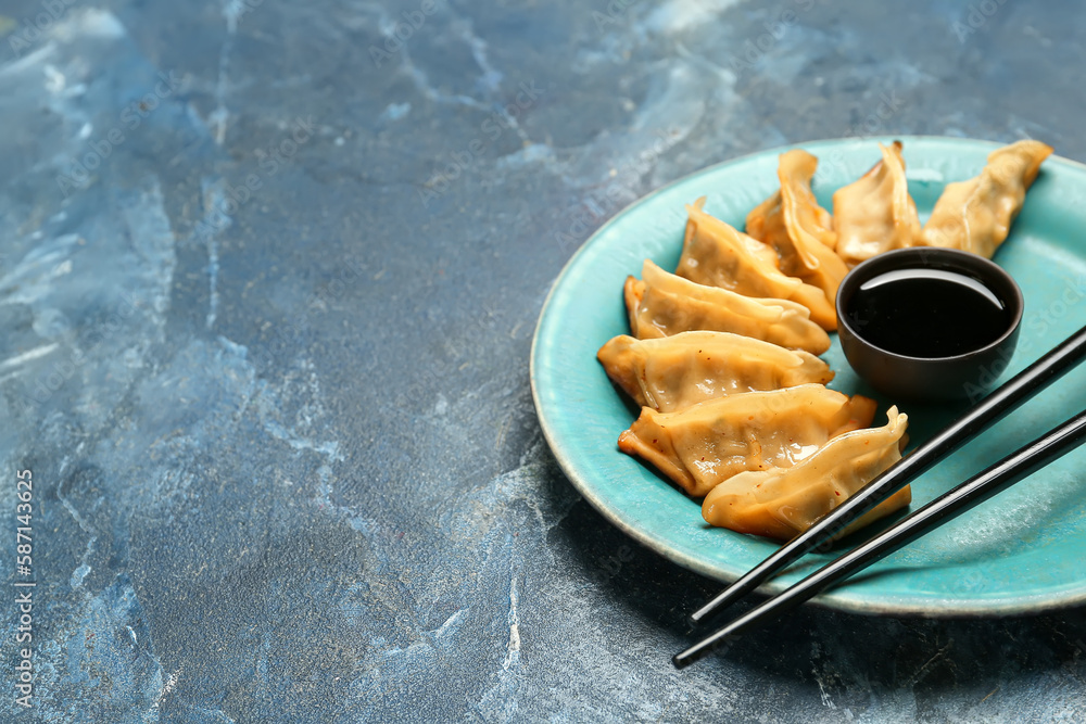 Plate with tasty Chinese jiaozi and sauce on blue background