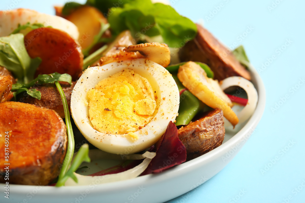 Plate of tasty potato salad with eggs and mushrooms on light blue background, closeup