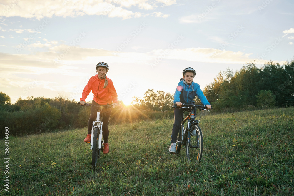 Mother and son ride a bike. Happy cute boy in helmet learn to riding a bike in park on green meadow 