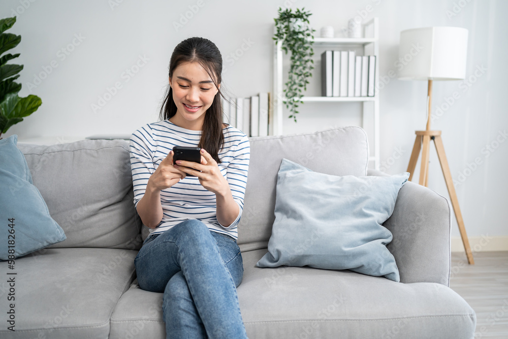 Asian beautiful woman sitting on sofa and swipe mobile phone in house. 