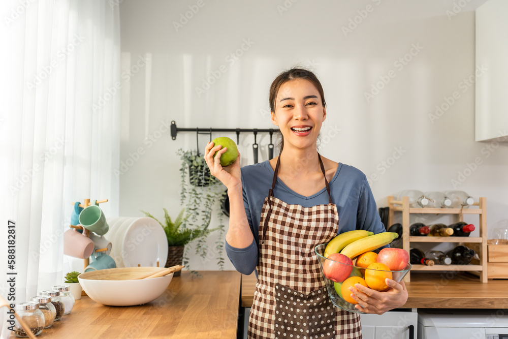 Portrait of Asian young woman hold a bowl of fruits and look at camera.