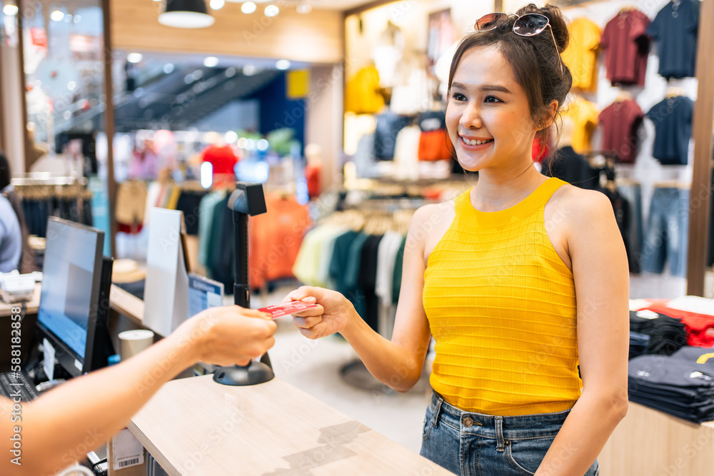 Asian young woman use credit card pay clothes product in shopping mall. 