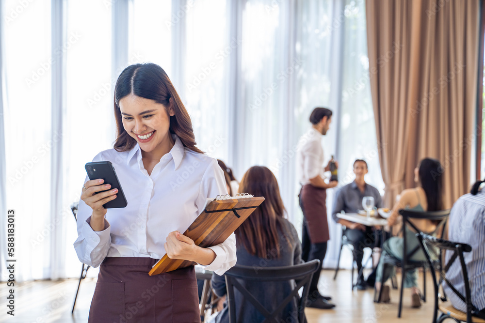 Asian beautiful waiter looking sale order on smartphone in restaurant. 