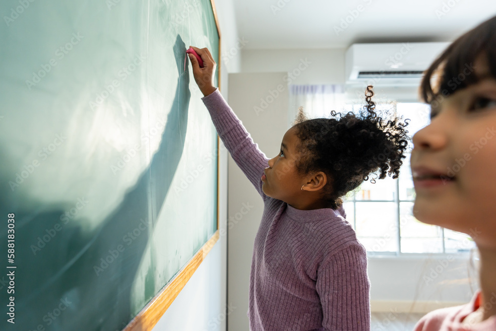 Diverse student writing blackboard in classroom at elementary school. 