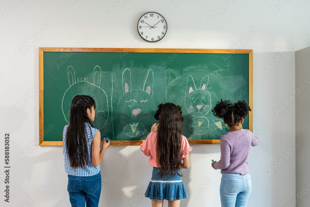 Diverse student writing blackboard in classroom at elementary school. 