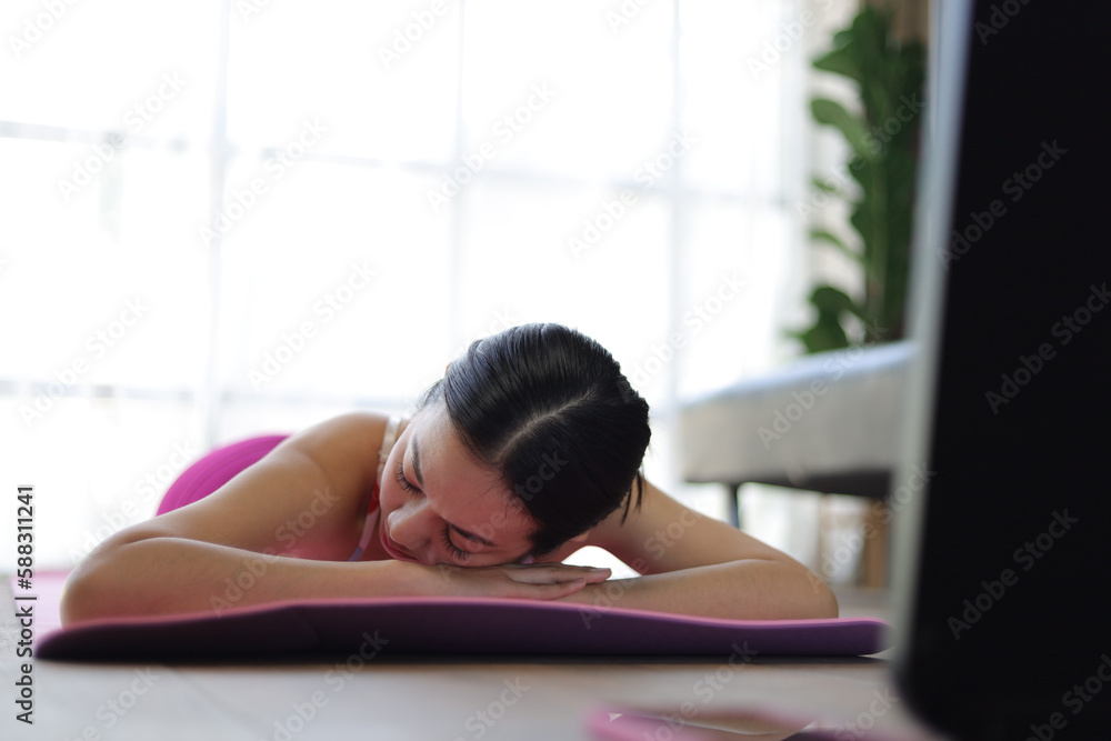 Beautiful Asian woman lying down on carpeted floor and doing yoga in living room at home.