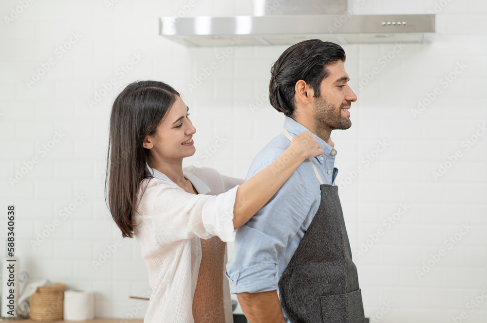 Happy couple cooking together in the kitchen at home, A couple wears apron to each other to make bre