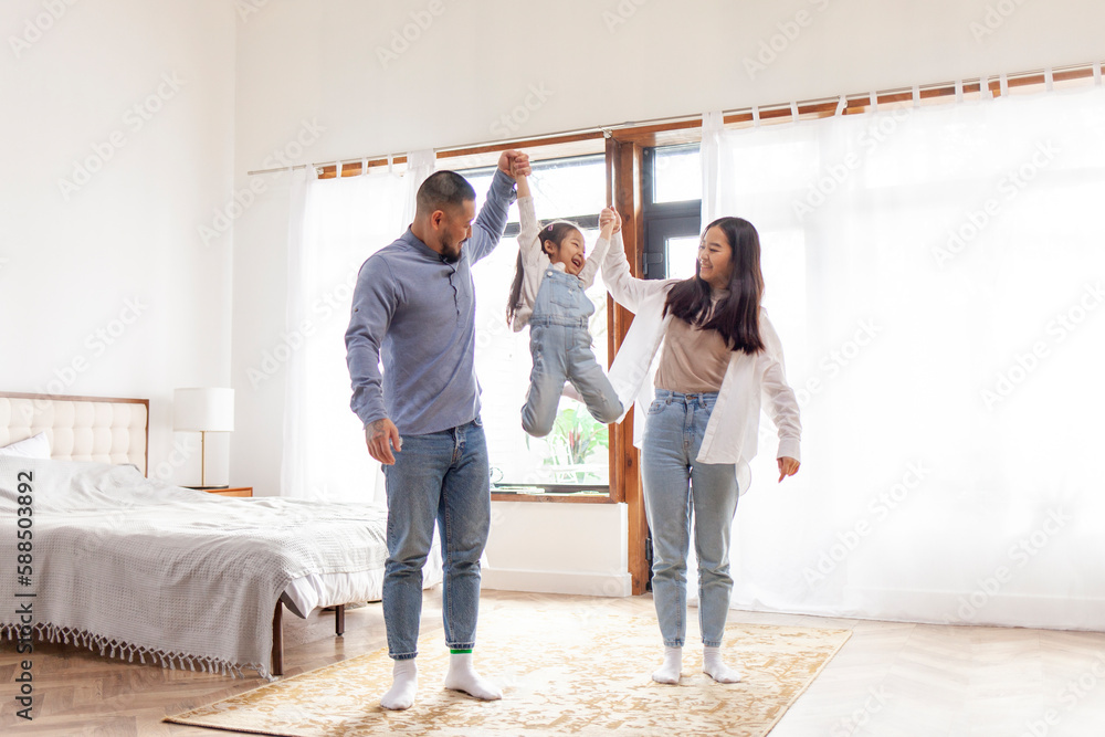 happy Asian family with little daughter stands at home in the bedroom and rejoices, dad and mom rais