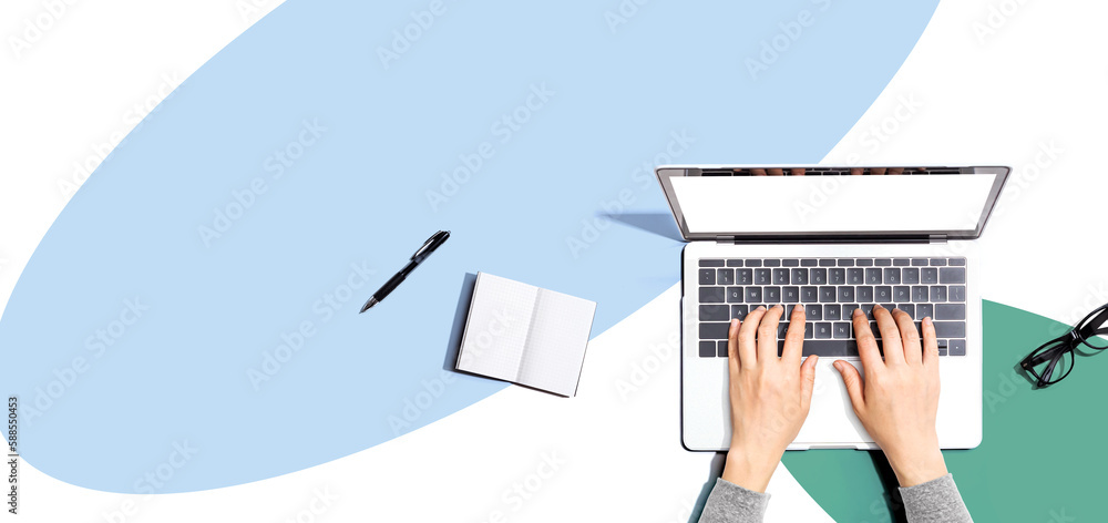 Person using a laptop computer with a notebook and eyeglasses - Flat lay