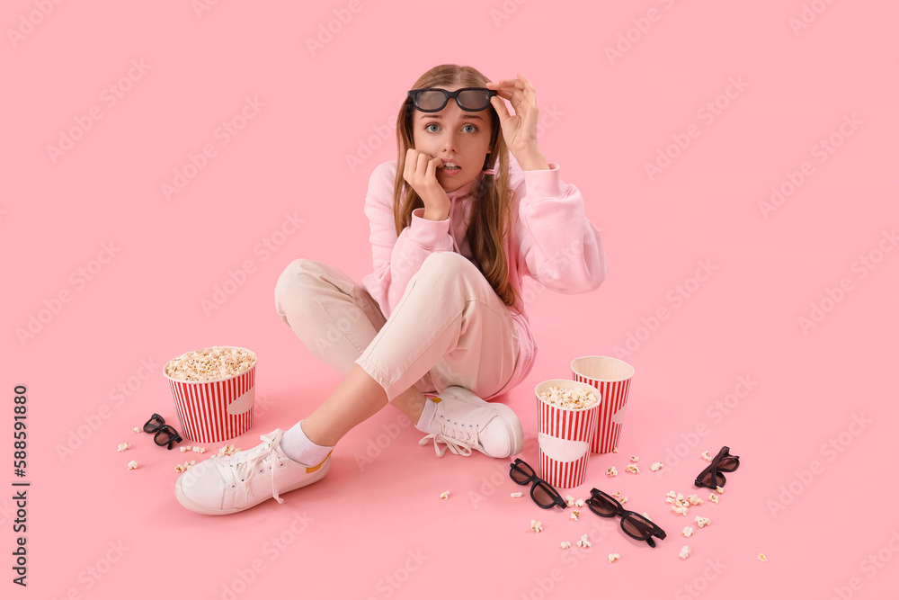 Young woman in 3D glasses with popcorn biting nails on pink background