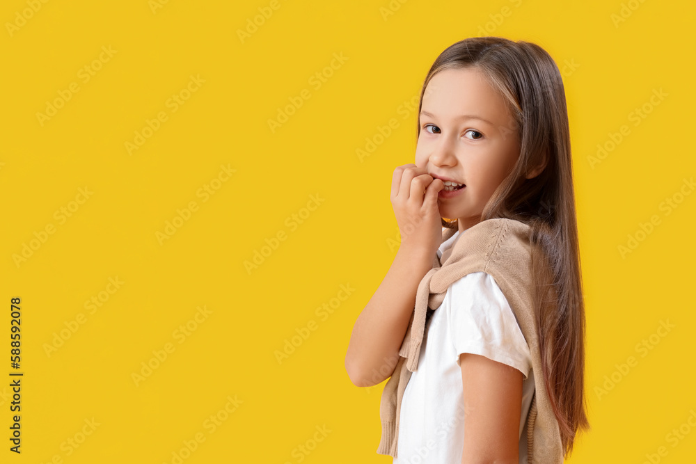 Little girl biting nails on yellow background