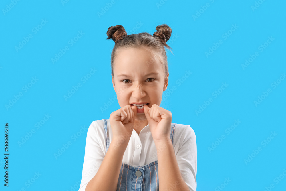 Little girl biting nails on blue background, closeup