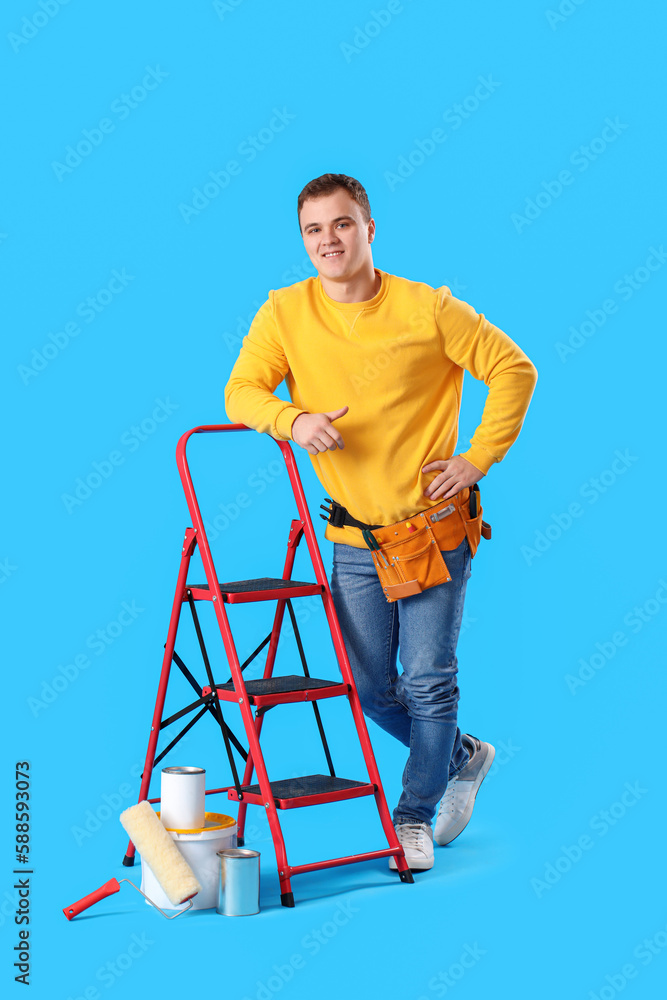 Young man with ladder and cans of paint on blue background