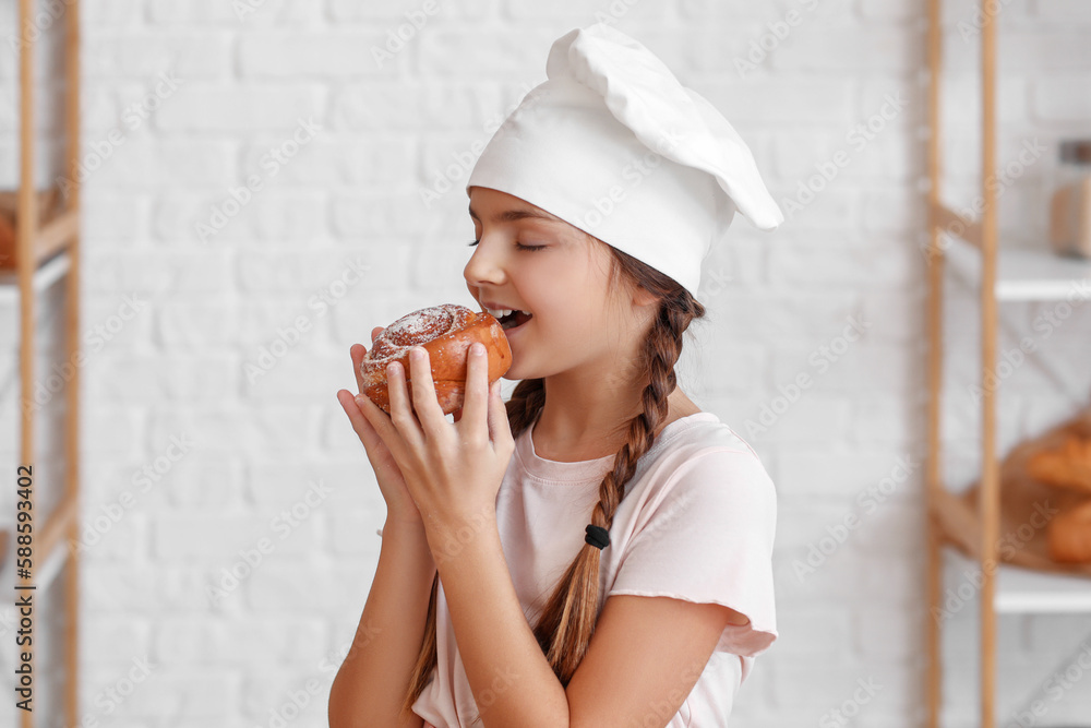 Little baker eating tasty bun in kitchen, closeup