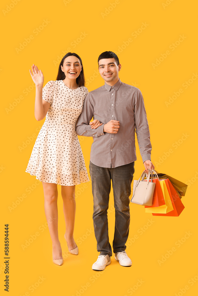 Lovely young couple with shopping bags walking hand in hand on yellow background