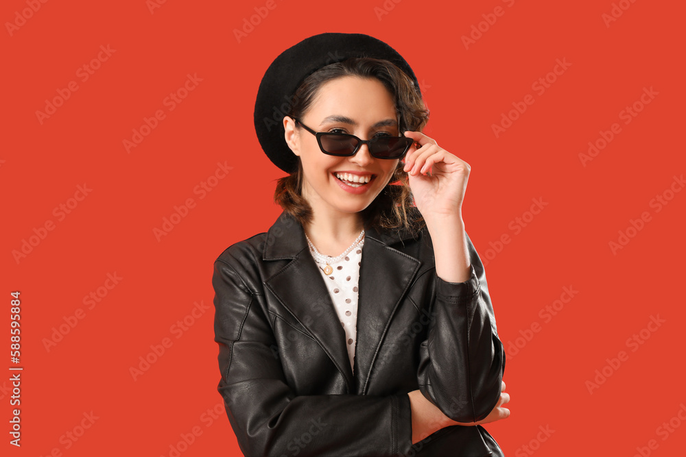 Stylish young woman in sunglasses on red background