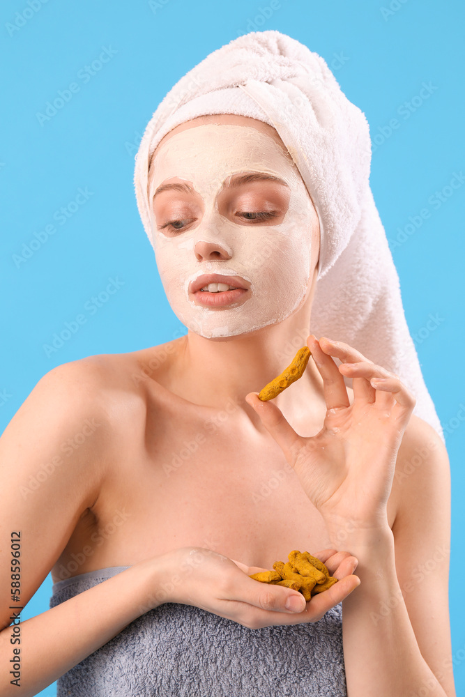 Young woman with applied turmeric mask and roots on blue background, closeup