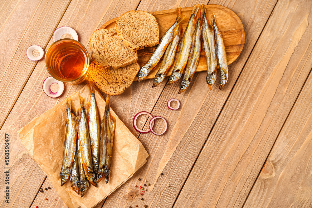 Delicious smoked capelin, glass of beer and bread pieces on wooden background