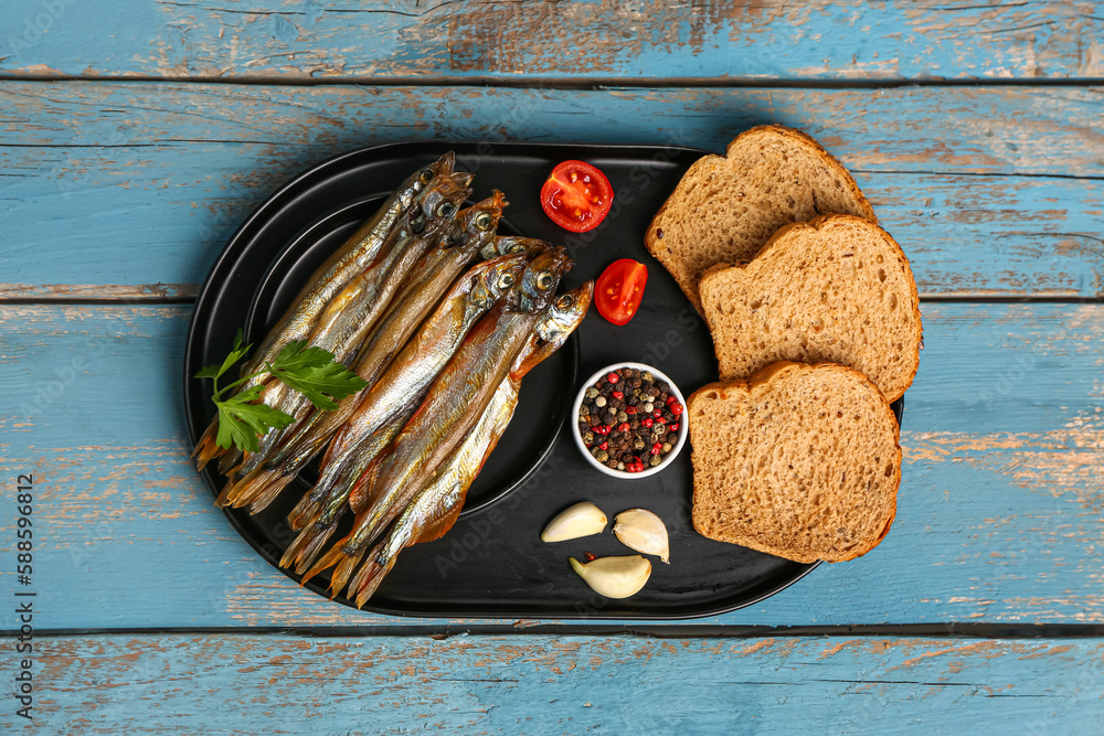 Board with tasty smoked capelin and bread pieces on blue wooden background