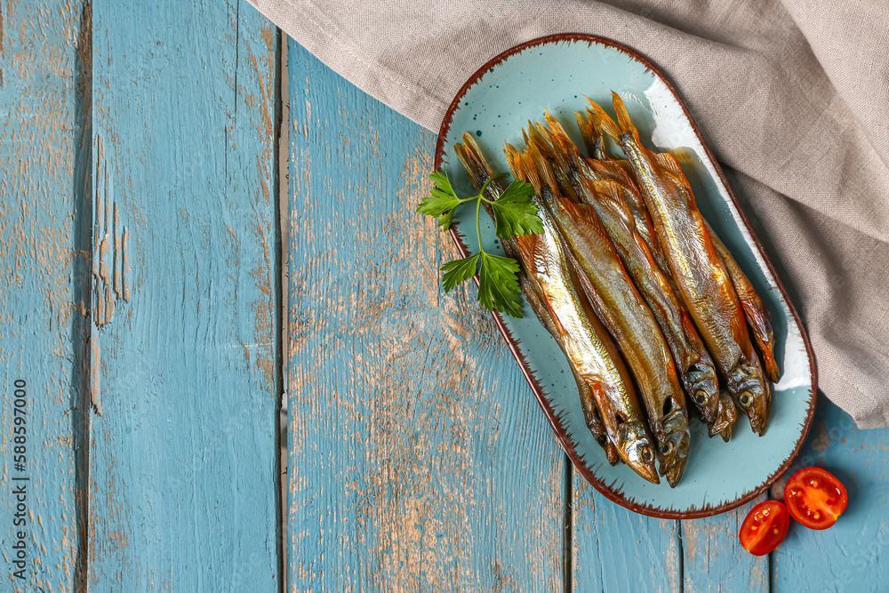 Plate with tasty smoked capelin on blue wooden background