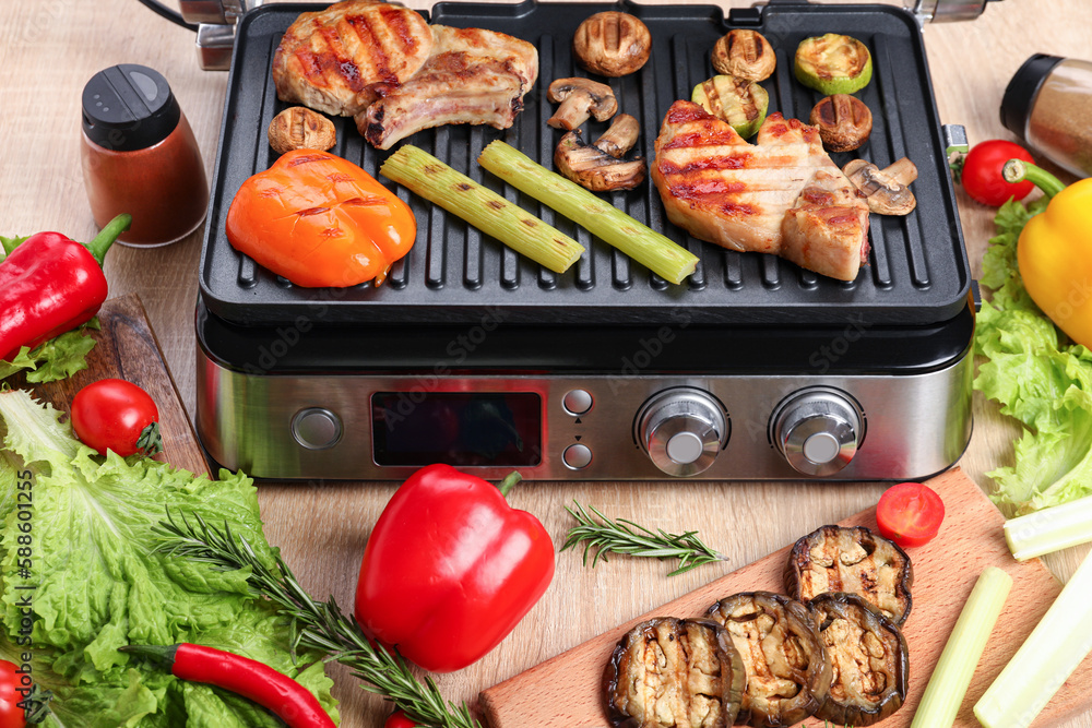 Modern electric grill with tasty steaks and vegetables on wooden background