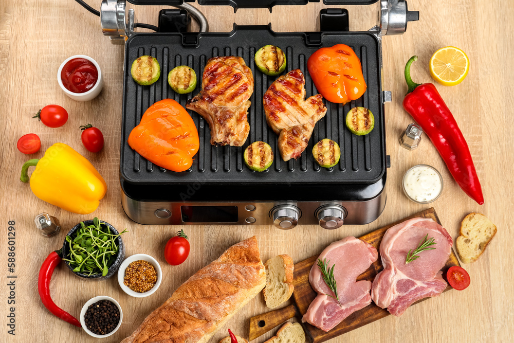 Modern electric grill with tasty steaks and vegetables on wooden background