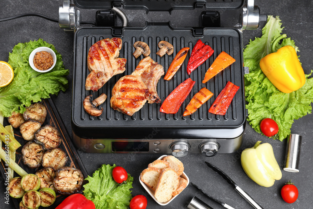 Modern electric grill with tasty steaks and vegetables on dark background