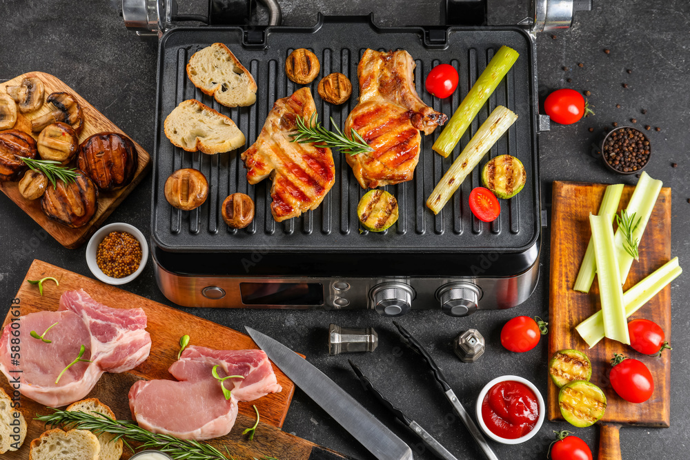 Modern electric grill with tasty steaks and vegetables on dark background