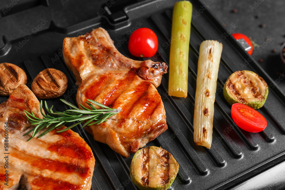 Modern electric grill with tasty steaks and vegetables on dark background, closeup