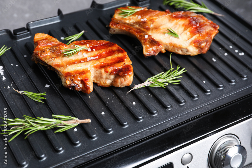 Modern electric grill with tasty steaks on dark background