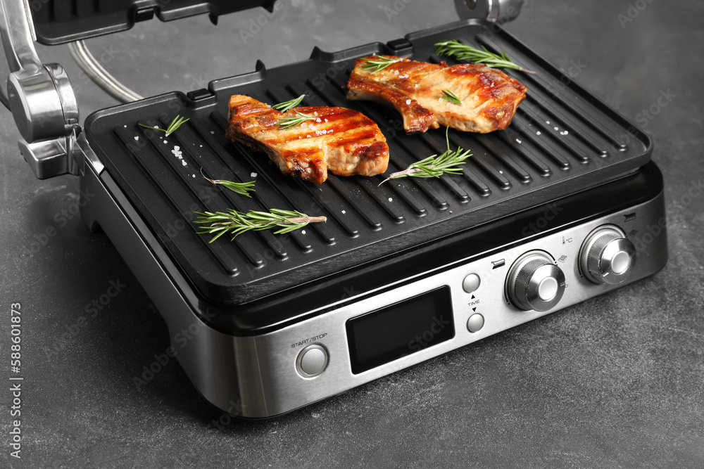 Modern electric grill with tasty steaks on dark background