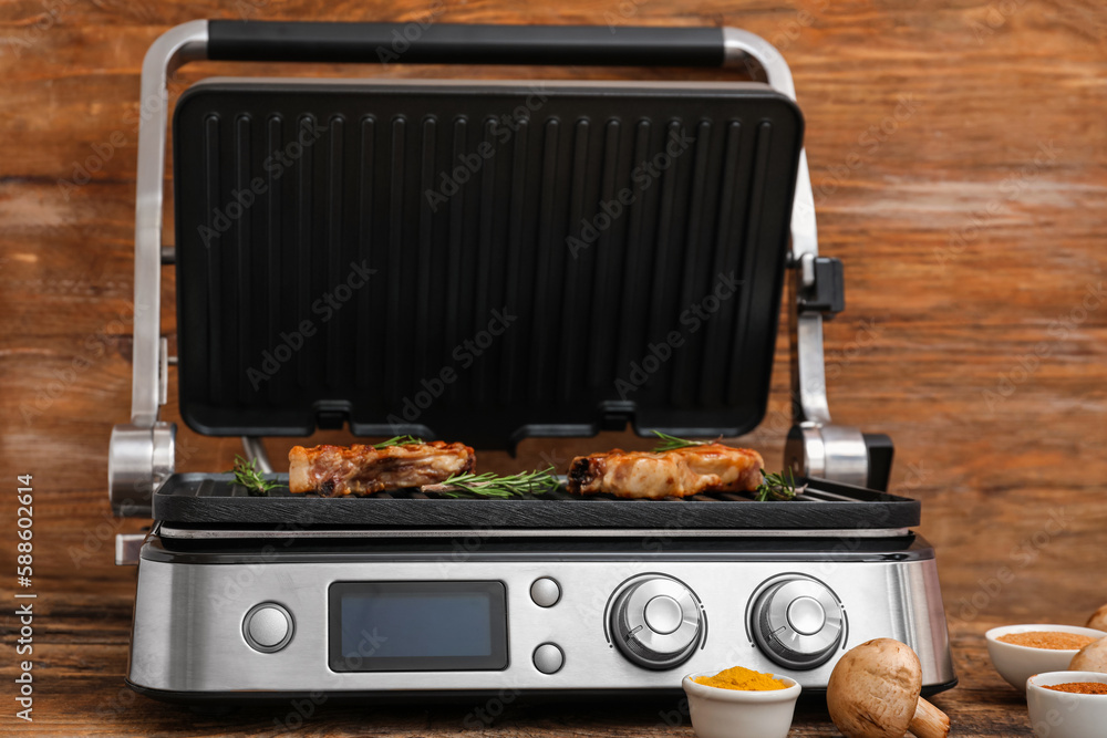 Modern electric grill with delicious steaks, mushrooms and spices on wooden table