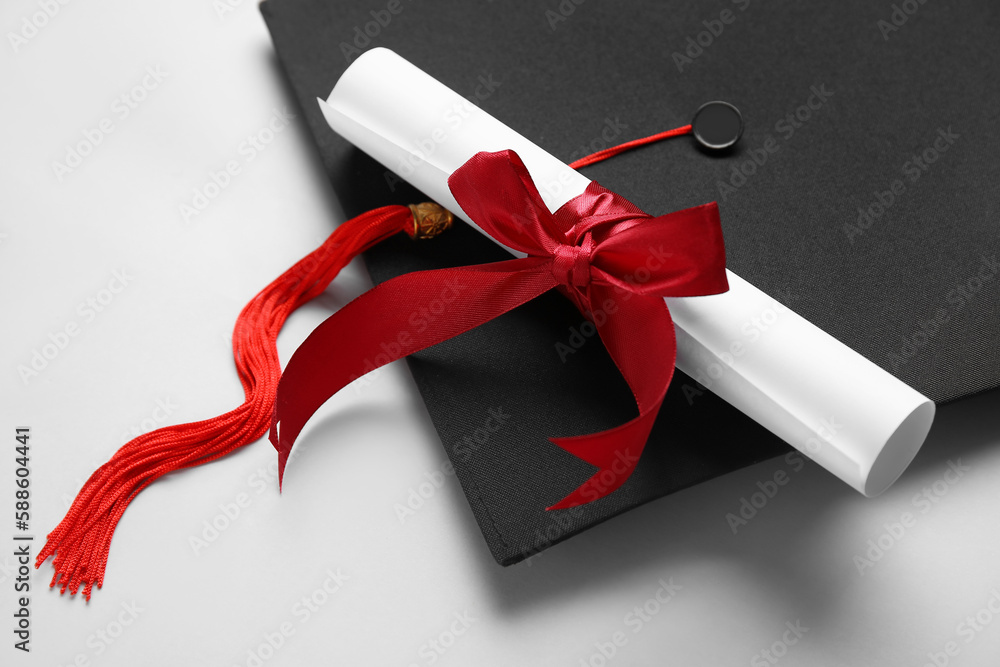 Diploma with red ribbon and graduation hat on white background