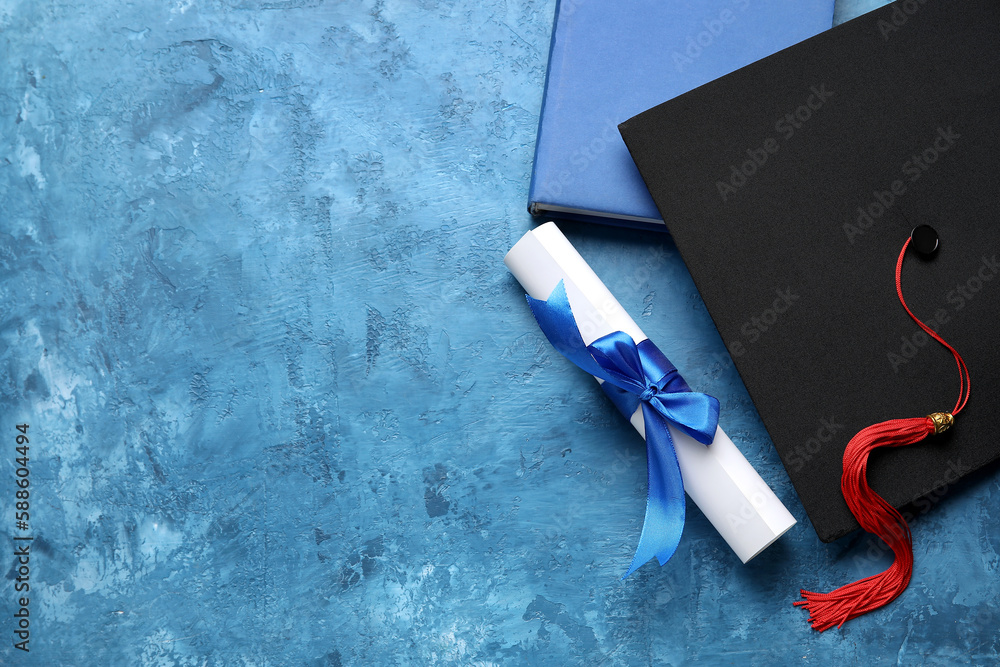 Diploma with ribbon, graduation hat and book on blue table