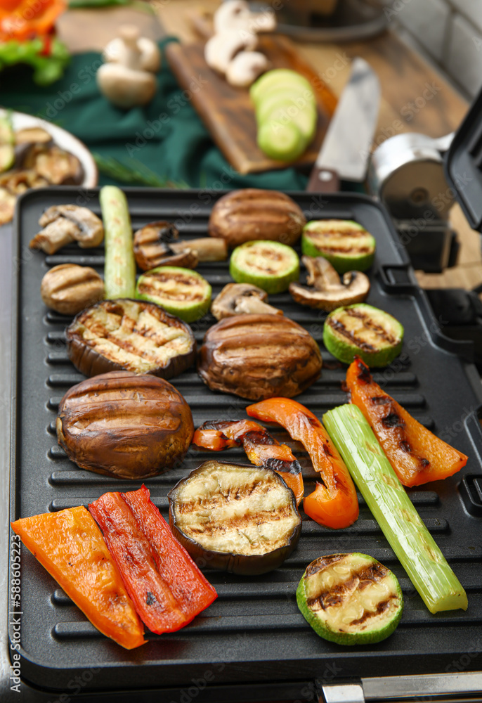 Modern electric grill with tasty vegetables on table in kitchen