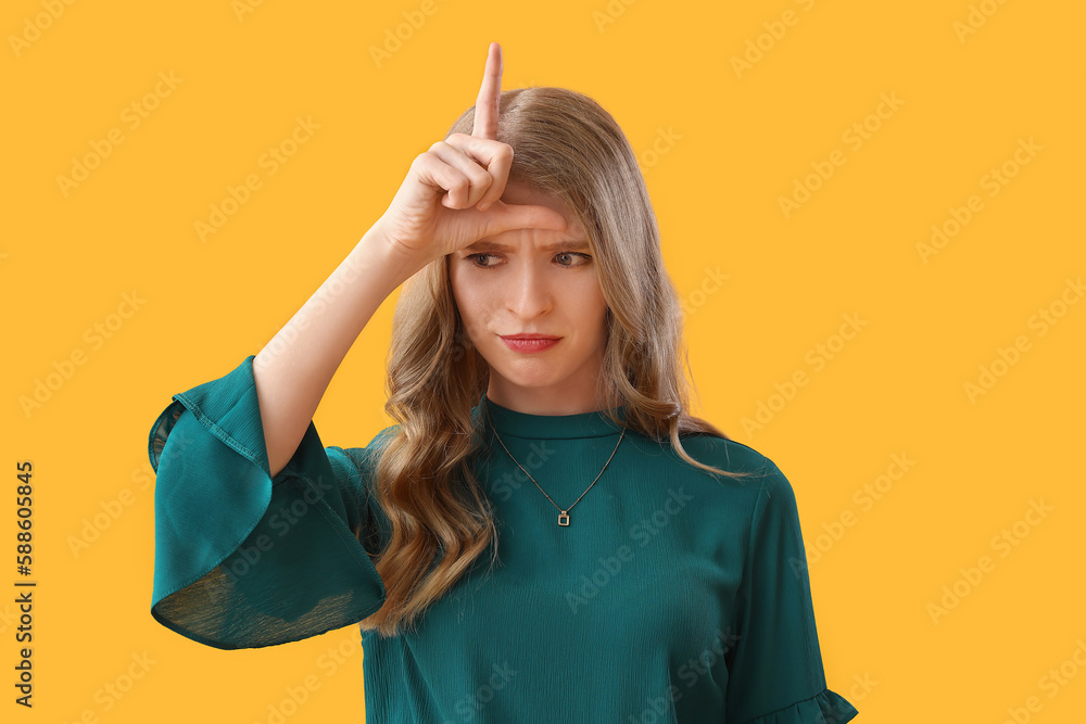 Upset young woman showing loser gesture on yellow background