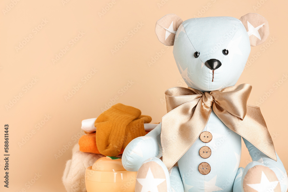 Toy bear with baby clothes on beige background