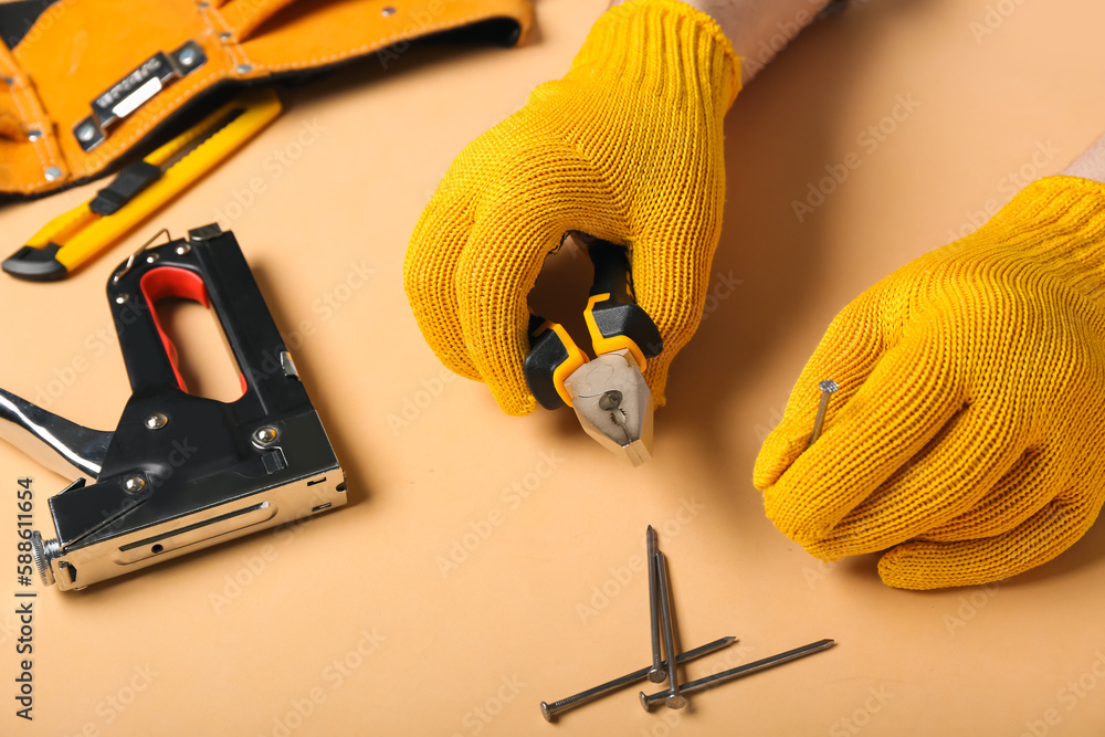 Male hands in gloves holding pliers and nail on beige background