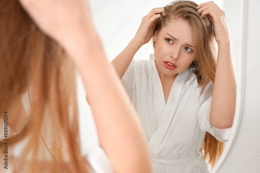 Worried young woman with hair loss problem looking in mirror at home