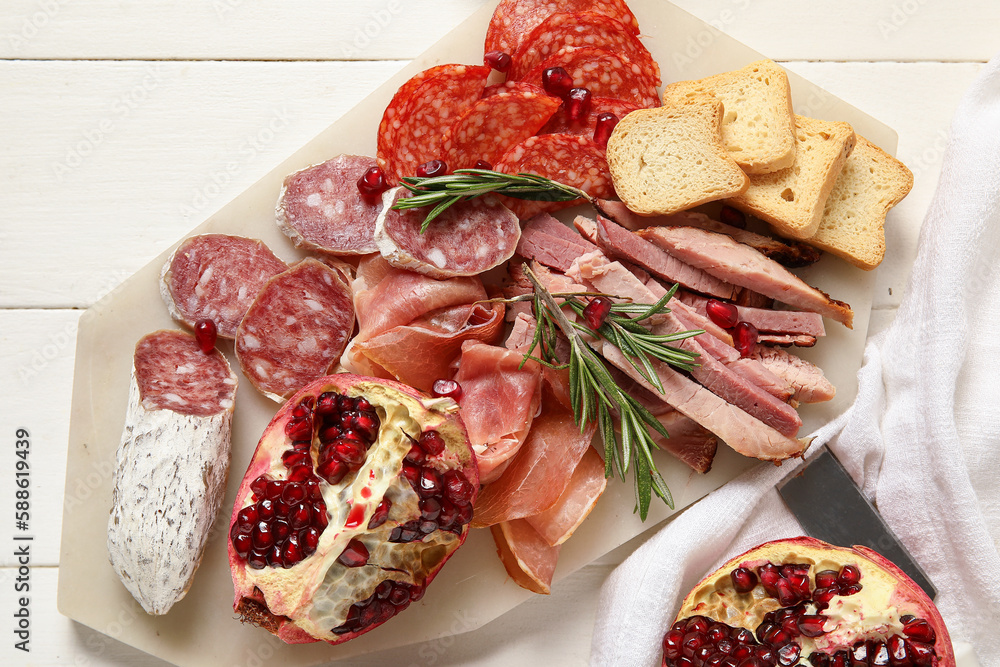 Board with assortment of tasty deli meats on white wooden background