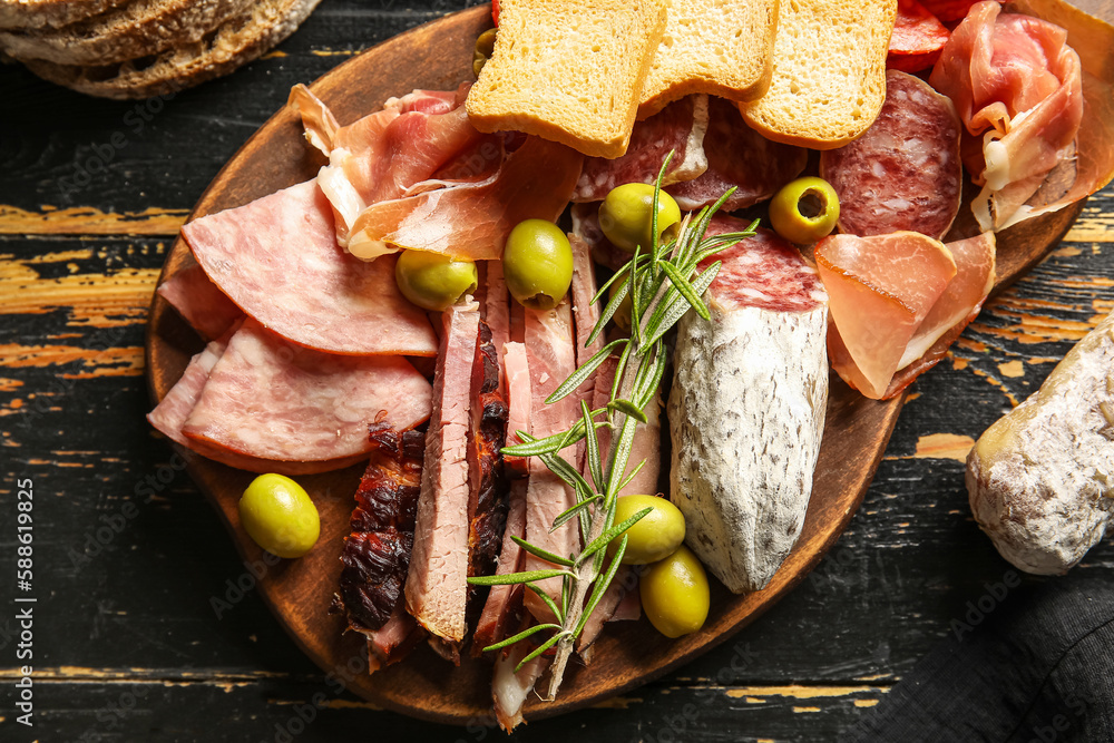 Board with assortment of tasty deli meats on dark wooden background