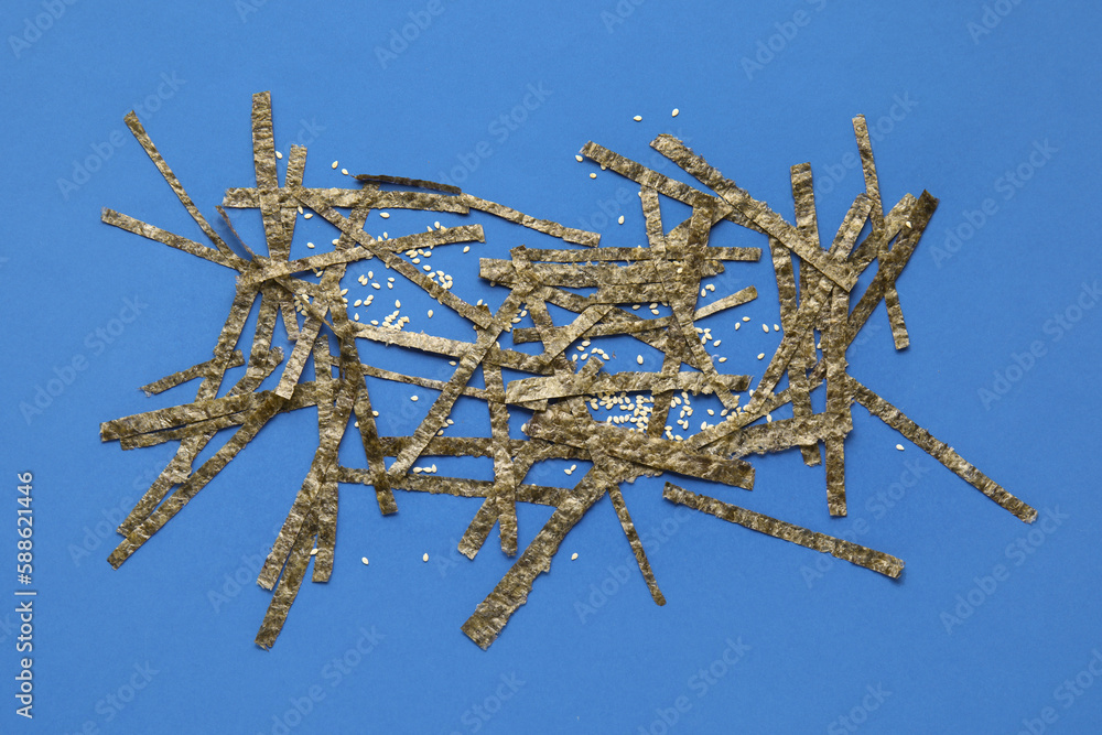 Cut nori sheets and sesame seeds on blue background